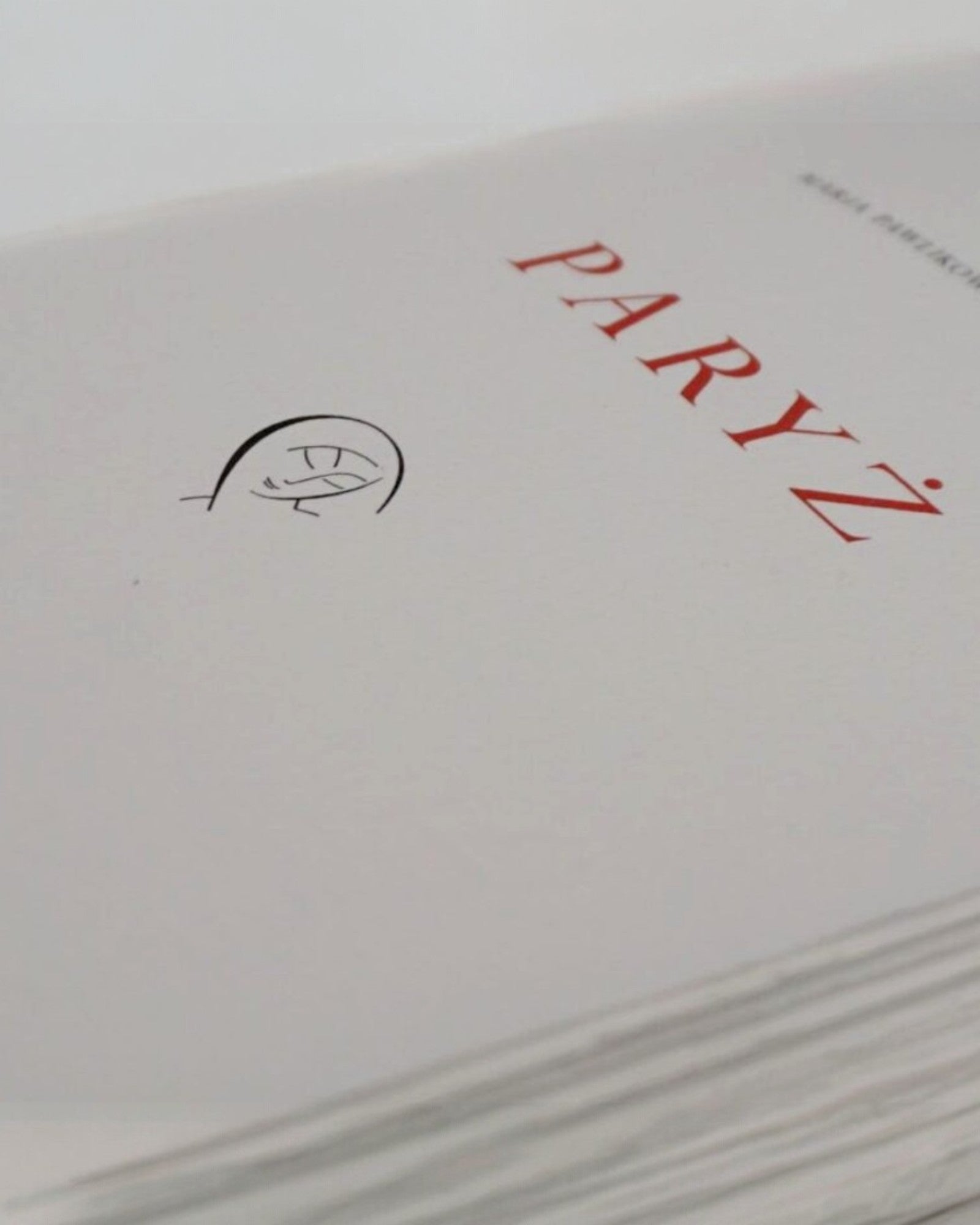 Zbliżenie strony tytułowej książki „Paryż” Marii Pawlikowskiej-Jasnorzewskiej z czerwonym napisem i minimalistyczną ilustracją na papierze bawełnianym.