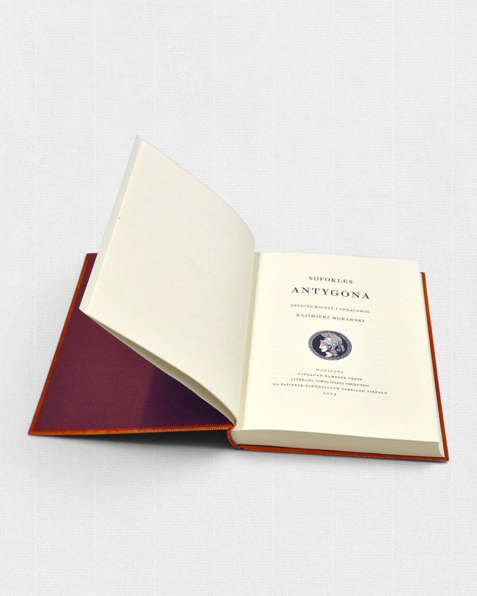 Antygona Sofoklesa – otwarta książka z widoczną stroną tytułową, wydrukowana na jasnym papierze i oprawiona w pomarańczową skórę.